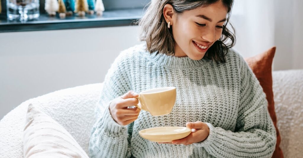 A cheerful young woman enjoying coffee while reading a book in a cozy living room.